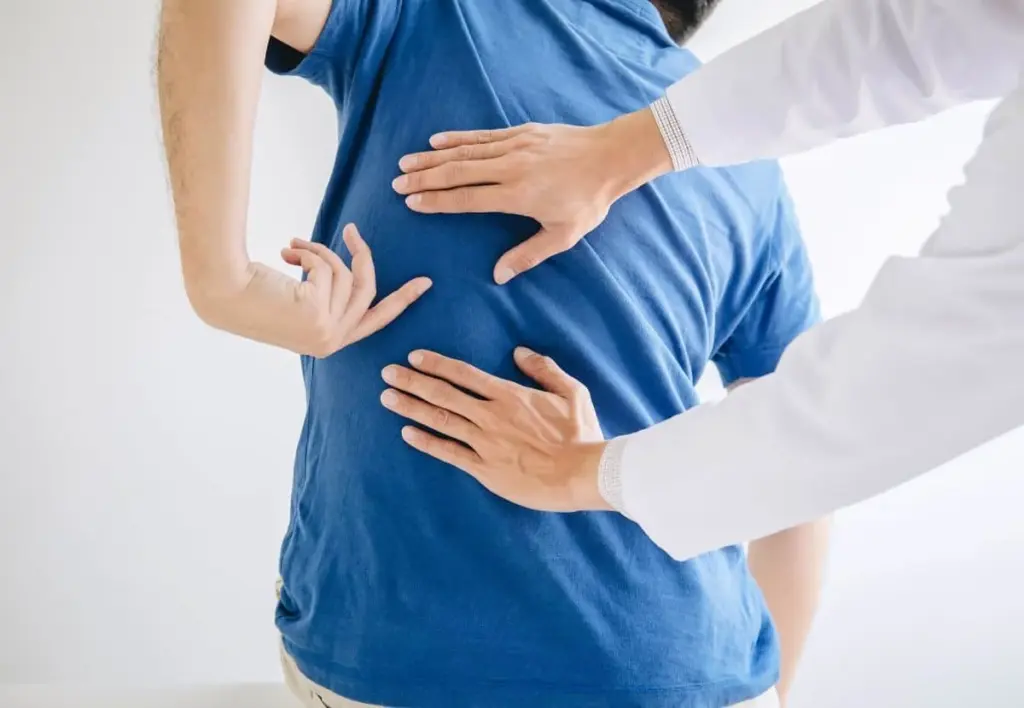 Clinician examining a standing patient's mid and lower back with both hands