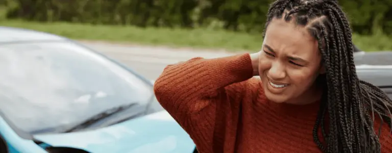 Woman holding her neck in pain beside a car after an accident