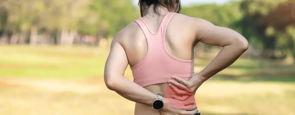Woman in running clothes holding her lower back outdoors