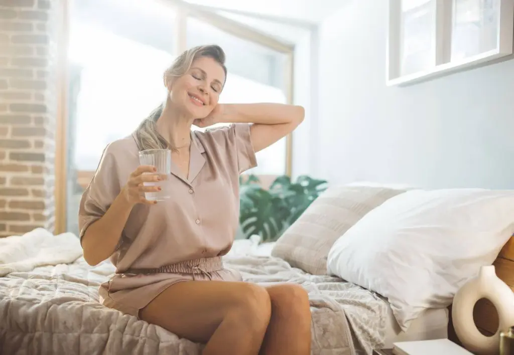 Woman stretching her neck while sitting on the edge of a bed