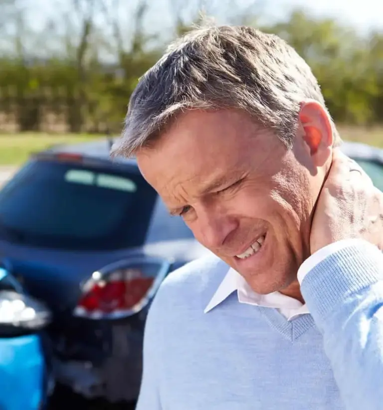Man wincing and holding his neck in front of a damaged car